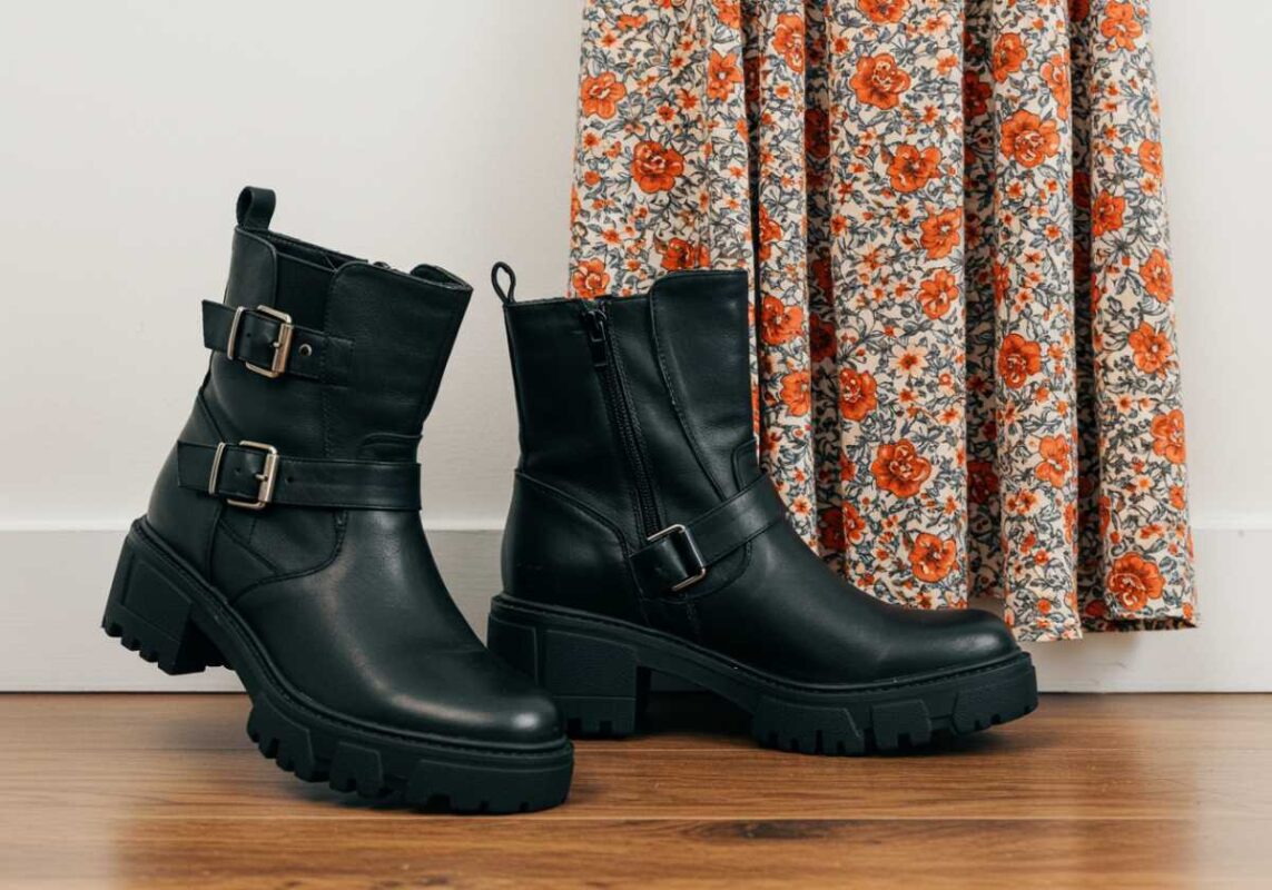 Black leather moto boots with buckles displayed next to floral bohemian dress showing style contrast.