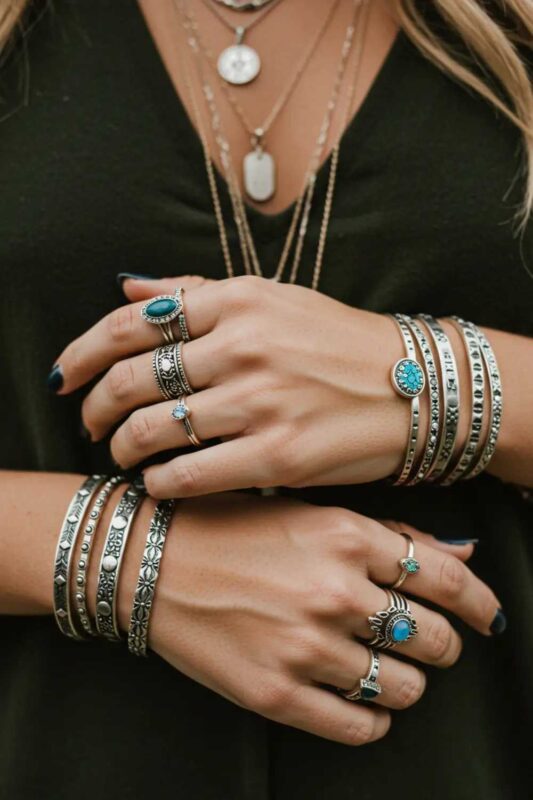 Close-up of a woman's hands adorned with stacked rings and layered bracelets—delicate and chunky designs with stones and subtle studs in Moto Boho style.