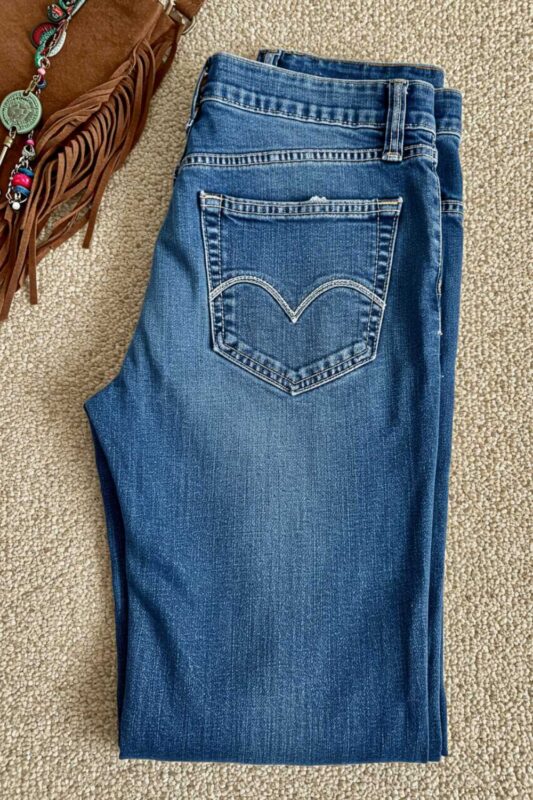 Worn-in vintage-style denim jeans folded with bohemian accessories showing versatility for Moto Boho styling.