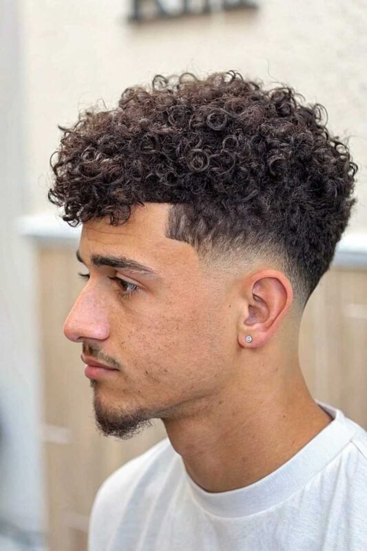Man with curly taper fade featuring clean sides transitioning into well-defined natural curls on top.