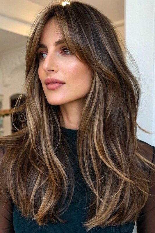 Woman with long layered hair and curtain bangs.