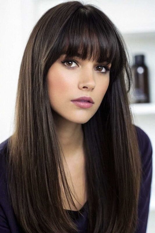 Woman with long straight hair and bold blunt bangs.