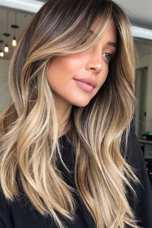 Woman with long hair featuring curtain bangs and balayage highlights.