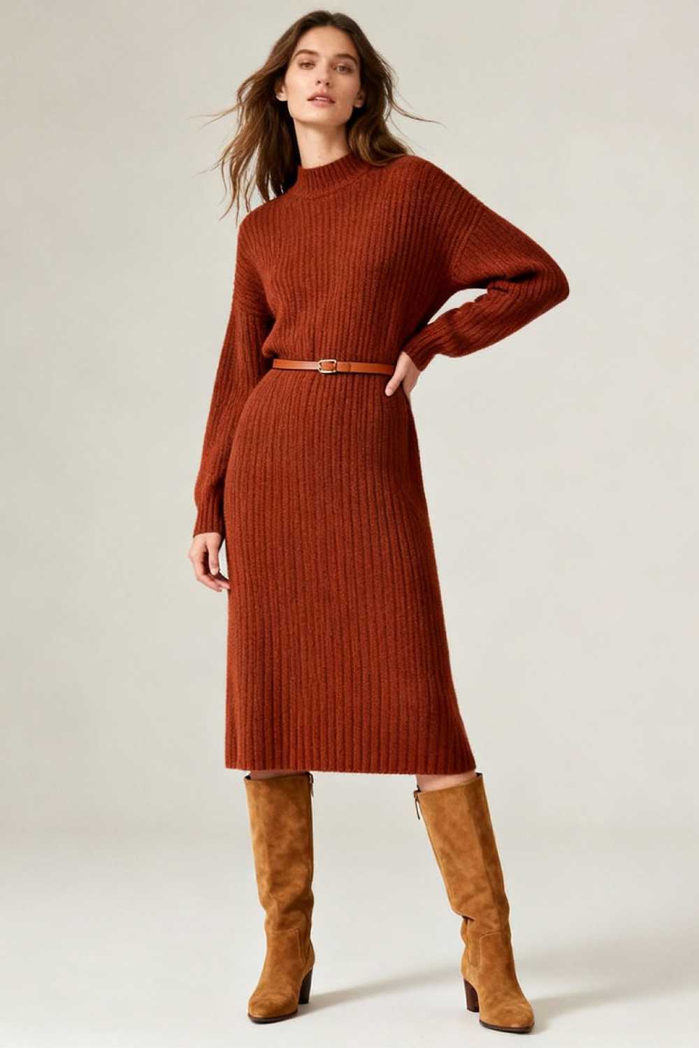 Fashion model in rust brown sweater dress with knee-high boots and belt in studio setting