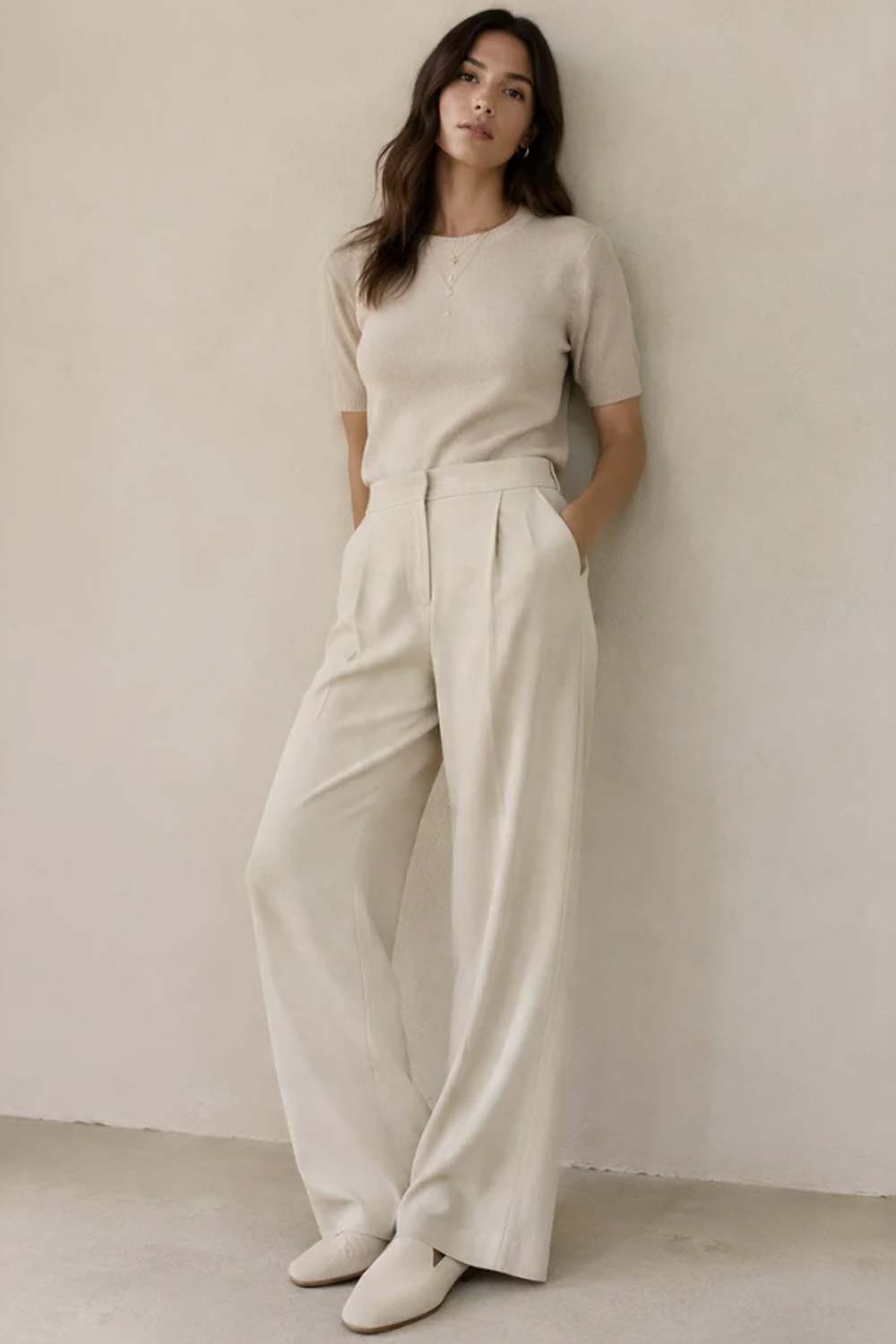 Woman in oatmeal monochrome outfit with cashmere knit sweater, wide-leg trousers, suede mules, and gold jewelry demonstrating tonal dressing